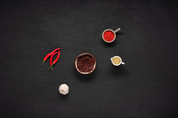 Ladjan in a sauceboat with ingredients: chili pepper, paprika, garlic, vegetable oil, on a black background top view