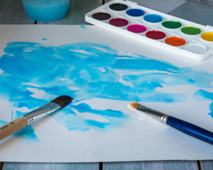 The beginning of the process of drawing watercolors in blue tones on a white sheet. Watercolor paints and sour closeup