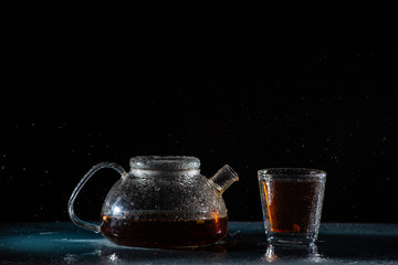 herbal sea black tea in a transparent teapot and in a transparent glass with a double bottom on a black background with splashes of water