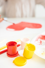 jars of paint yellow, red and white on the background of a blurry painting of a child