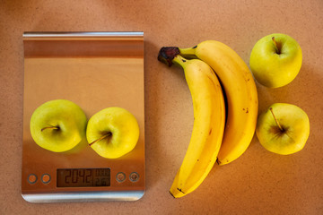 apples on a digital kitchen scale and beside are bananas and apples