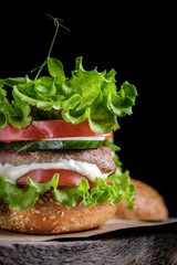 Homemade hamburger with fresh green leaf of salad, tomato and cucumber  on wooden table at black background