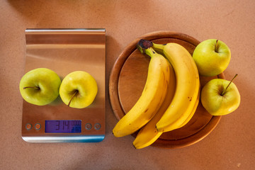 apples on a digital kitchen scale and beside are bananas and apples