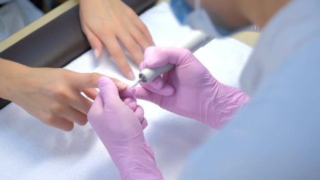 Manicurist woman removes gel shellac polish from client's nails using manicure machine, hands closeup. Manicure master is working with electric nail drill in beauty salon. Hardware manicure process.