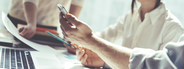 Group of young business people working together. Loft office and smart casual dress code. Researching new product strategy. Electronic devices and paperwork on the table. Wide screen panoramic