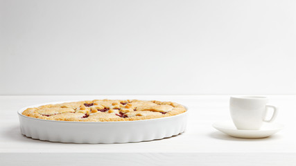 Homemade shortcrust cherry pie and white cup of coffee espresso on white wooden table. Front view. Copyspace.