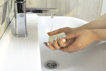 Girl with a beautiful manicure washes her hands with soap in the bathroom