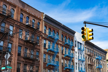 Row of Old Buildings with Blue Fire Escapes in Harlem of New York City and a Yellow Street Light - obrazy, fototapety, plakaty