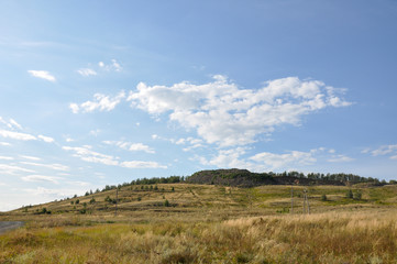 Bright landscape with mountains, tracks and summer house. Light blue sky with white clouds and deep green forests. Travelling 