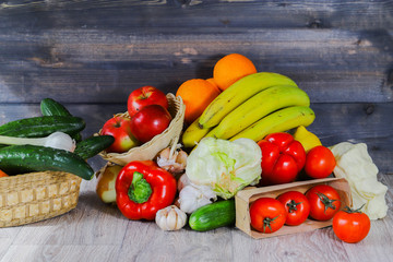 On a gray graphite wooden background, tomatoes in a box, cucumber, garlic, large red peppers, bananas, oranges, red apples in a wicker plate, cucumbers and garlic in a basket.