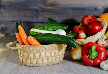 On a gray graphite wooden background, tomatoes in a box, cucumber, garlic, large red peppers, bananas, oranges, red apples in a wicker plate, cucumbers and garlic in a basket.