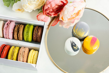 colorful modern macaroons in gift box in female woman hands and on plate for celebration romantic party birthday, pion flowers, satin ribbon, many different types flavors of macaron. Gentle flat lay 