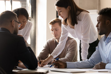 Multicultural businesspeople gather at office table brainstorm discuss paperwork together at...