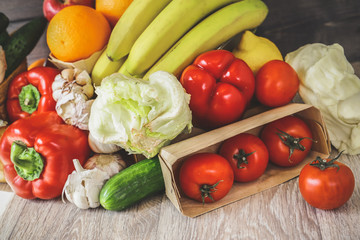 Close-up in a box of tomatoes, next to the table are cucumber, garlic, Iceberg salad, large red peppers, bananas, oranges.