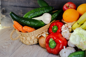 Fresh vegetables and fruits, in a basket bright young carrots, cucumbers, fresh garlic, red peppers, garlic on the table. Salad, bananas, oranges and red apple.