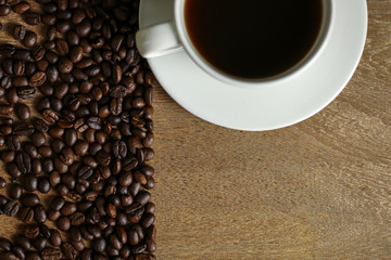 White coffee cup and coffee beans on wooden table with copyspace for text. Selective focus.