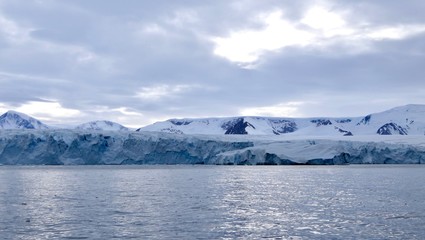 Fototapeta na wymiar Glacier front in antarctic sea with cloudy sky, ocean with light reflections, Antarctica