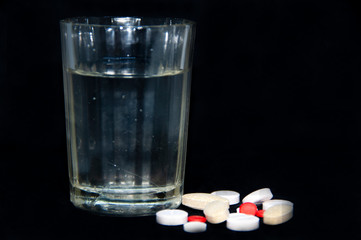 glass of water and pills. pills on a black background.