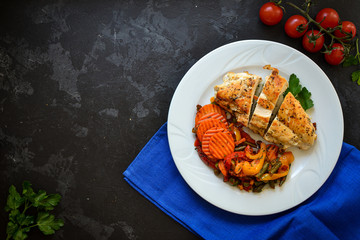 Baked chicken breast with vegetables. Chicken breast, asparagus, carrots, in a white plate. Top view. Dark background. Free space for text. Blue linen napkin.