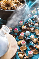 A close up of essential oils, potpourri  and a diffuser vaporizing aromas over a green linen scarf