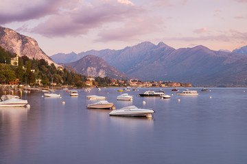 Fototapeta na wymiar Lake Maggiore at sunrise, Italy. Panorama from the lakefront of the town of Stresa towards Baveno with boats and silk water effect