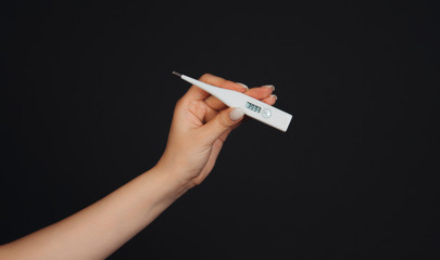 white thermometer in a female hand on a black background with high temperature