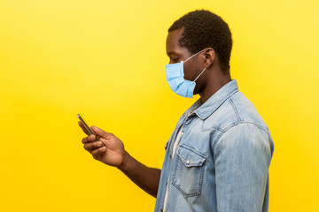 Side view of serious attentive man with surgical medical mask holding cellphone, typing or dialing number or reading news and looking at screen. indoor studio shot isolated on yellow background