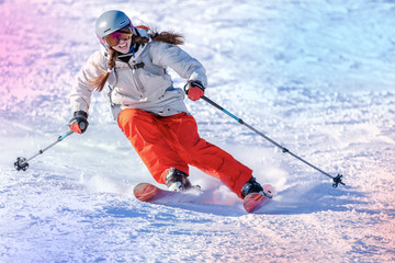 Girl On the Ski. a skier in a bright suit and outfit with long pigtails on her head rides on the track with swirls of fresh snow. Active winter holidays, skiing downhill in sunny day. Woman skier