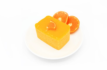 Orange cake with a piece of orange on topping and blurred slices of orange in white dish or plate isolated on white background. Sweet or Dessert food and Ready to eat concept