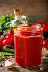 Homemade tomato sauce with basil, garlic and fresh tomatoes. Ketchup, marinara sauce in small jars. On a wooden background, with fresh vegetables and basil.