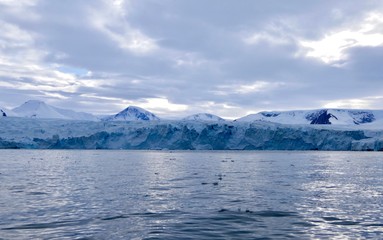 Fototapeta na wymiar Glacier front in antarctic sea with cloudy sky and ocean with light reflections, Antarctica