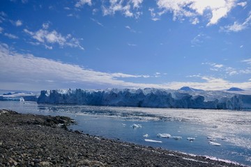 Glacier front with stone beach landscape in Antarctica, blue sky and sun, Stonington Island