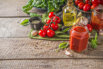 Homemade tomato sauce with basil, garlic and fresh tomatoes. Ketchup, marinara sauce in small jars. On a wooden background, with fresh vegetables and basil.