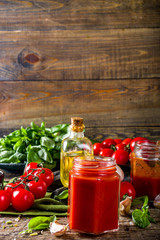 Fototapeta na wymiar Homemade tomato sauce with basil, garlic and fresh tomatoes. Ketchup, marinara sauce in small jars. On a wooden background, with fresh vegetables and basil.