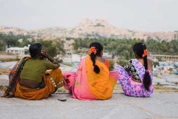 Mujeres indias sentadas contemplando el paisaje de Hampi, India. Van vestidas con el Sari colorido y tienen el pelo largo con flores naranjas en el cabello.