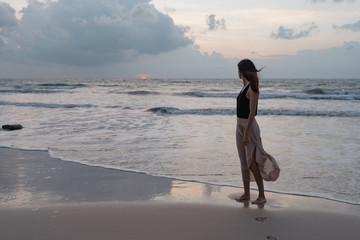 Chica mirando la salida del sol en una playa de la India en un dia con viento.