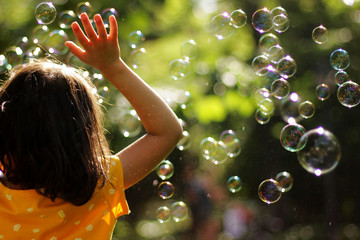 niña de espalda en el parque jugando con burbujas de jabón
