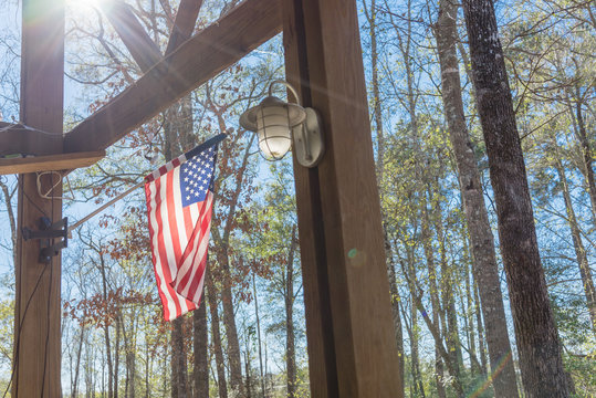 American flag flying on pole with wall lamp on patio of cabin at nature park near of Houston, Texas - Powered by Adobe