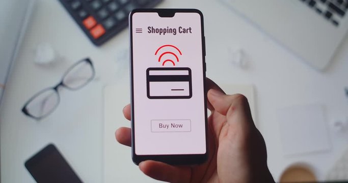 Buying goods in online store using smartphone application. Pressing the Buy Now button to shop and pay a online store on smartphone. BUY NOW button being pressed on a smartphone screen
