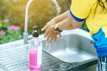 A woman washing hands from the tap with pink soap in a aluminium tub. Concepts of Flu virus, Covid-19 (Coronavirus disease). Selective focus on soap bottle.
