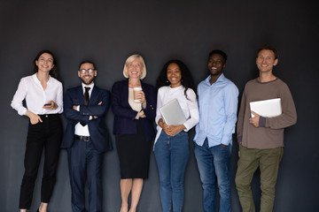 Group picture of smiling multiethnic diverse businesspeople stand posing near black wall look at...