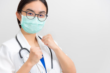 Beautiful Asian young woman doctor in white uniform and mask protect Coronavirus, Physician raise fists to support patient in the fight against disease epidemic COVID 19, gray copy space background