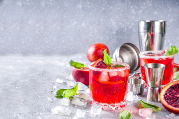 Skinny blood orange basil lemonade cocktail, with fresh bloody oranges, basil leaves and vodka, Grey stone concrete background flat lay copy space