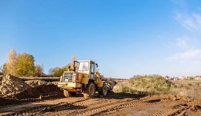 Fototapeta premium large yellow wheel loader aligns a piece of land for a new building. Preparation of the land for the auction. Leveling the landscape and adding sand for construction.