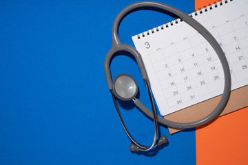 Top view of stethoscope and calendar on the blue and orange background, schedule to check up healthy concept