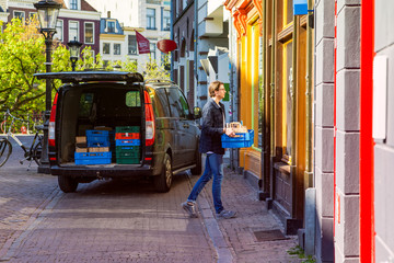 Local restaurant delivering catering service, black transport car dropping of wine and food at a home young entrepreneur walking to a home