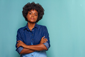 Black young woman with glasses with black power hair wearing blue jeans shirt on blue background, serious