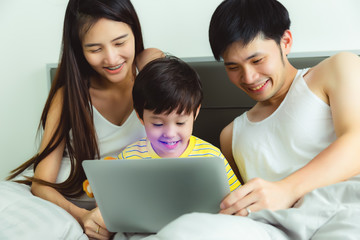 Happy family. Father mother son watching movie on laptop computer in bed at bedroom with happiness, laughing. Family stay at home together. Lovely little Child get warm and happy when stay with parent