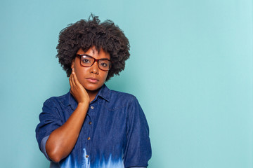 Obraz na płótnie Canvas Black young woman with glasses with black power hair wearing a blue jeans shirt on blue background