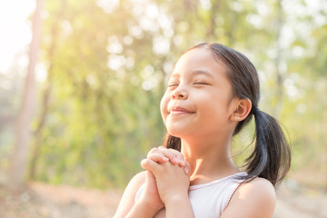 cute little girl hands praying to god with the bible in the morning on nature background.  little asian girl hand praying for thank god. copy space. spirituality and religion faith hope concept.